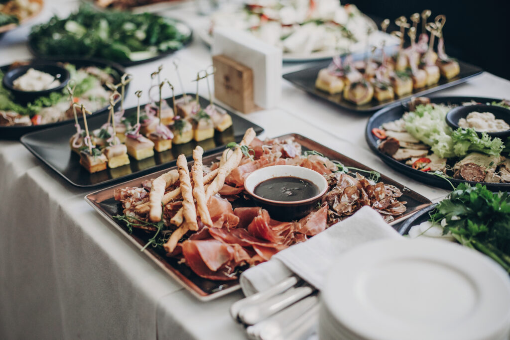 Smoked meat,sauce,prosciutto, salad appetizers on table at wedding or christmas feast. Luxury catering concept. Delicious italian food table at wedding reception.